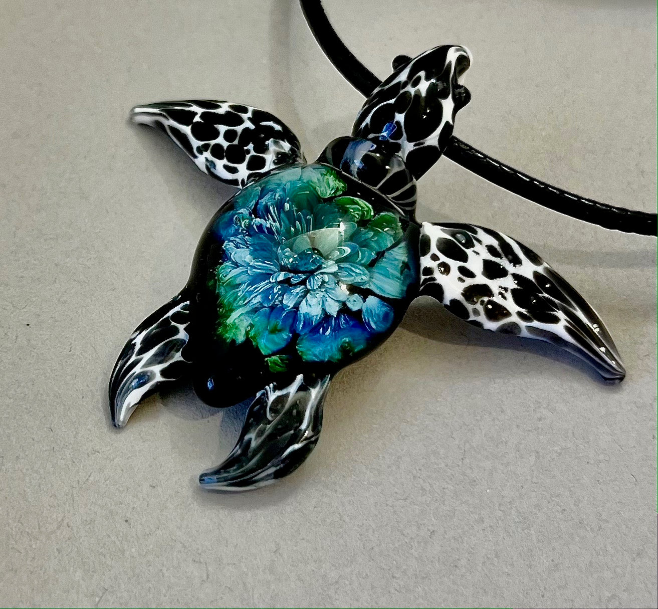 glass black and white spotted sea turtle pendant with iceberg style explosion in the shell at a 60 degree angle. 