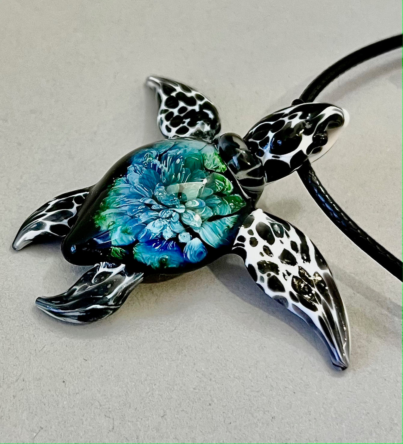 glass black and white spotted sea turtle pendant with iceberg style explosion in the shell at a 45 degree angle.