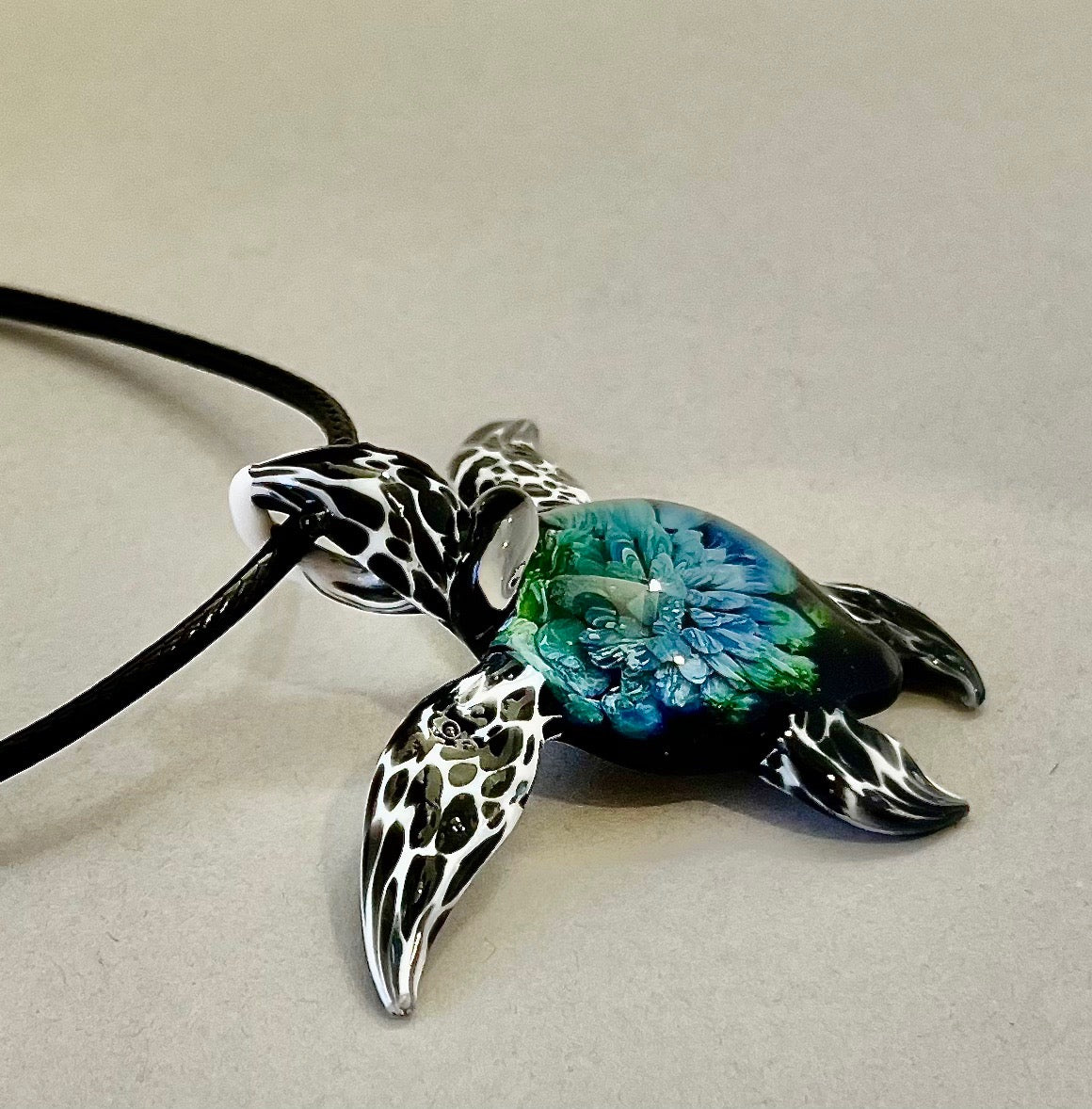 glass black and white spotted sea turtle pendant with iceberg style explosion in the shell at a 180 degree angle.