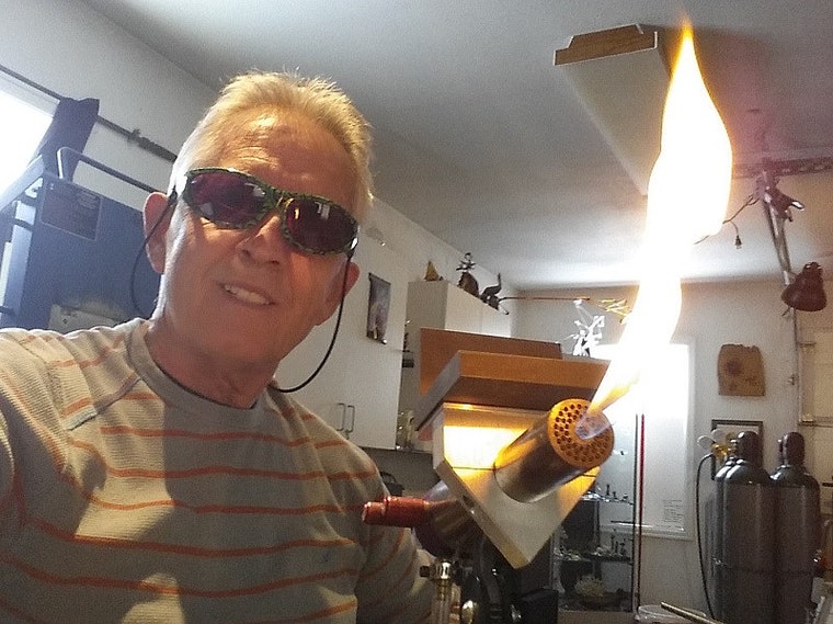 Glass artist Ron Murphy beside a lit glassworking torch in his studio